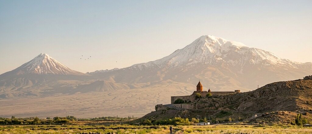 A walled monastery on a low hill, with a snow-capped twin-peaked mountain behind it